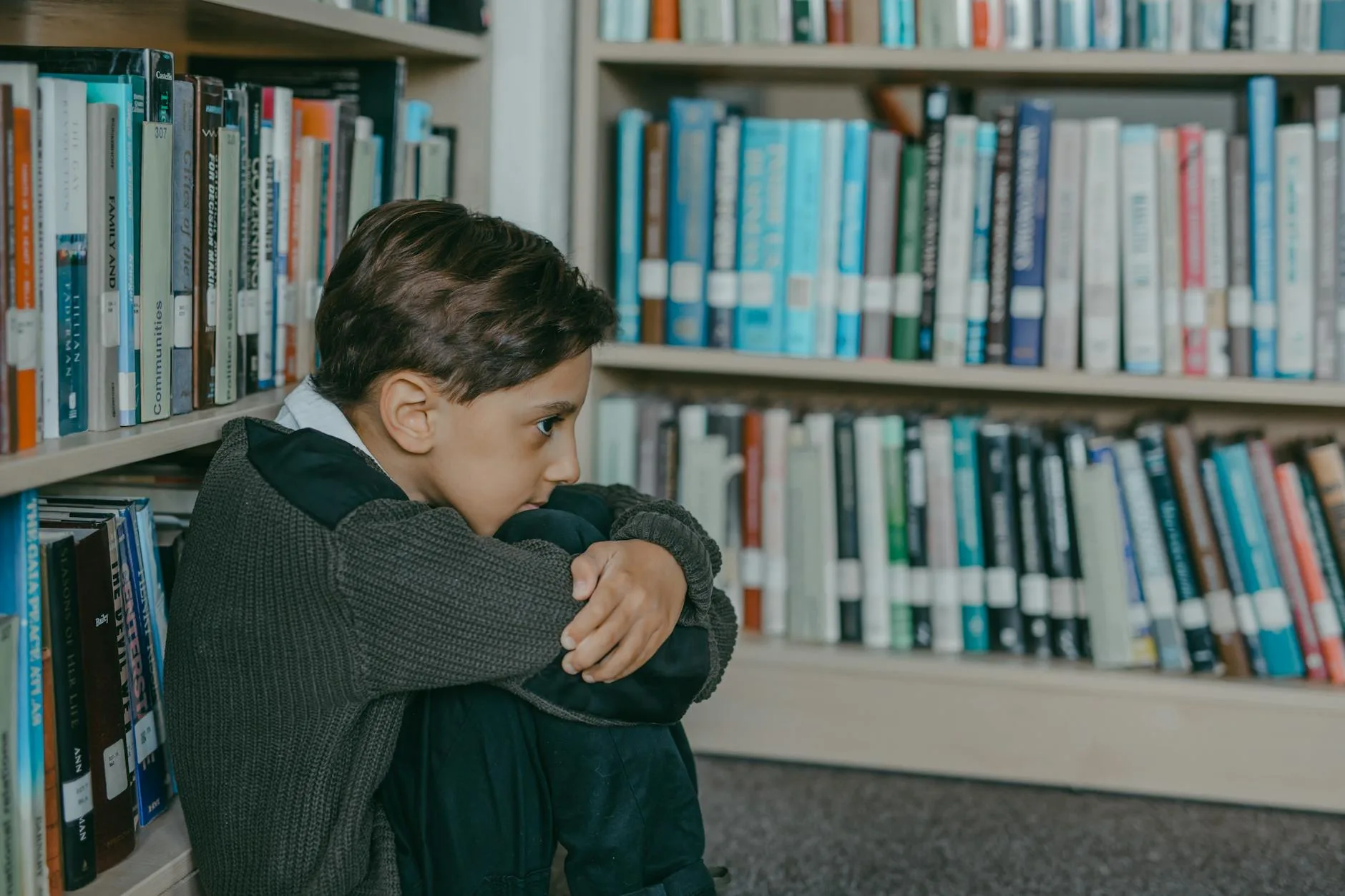 Chłopiec zamyślony w bibliotecznym kąciku otoczony książkami